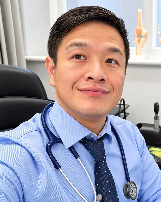 Dr Chun Tang at his desk in clinic, wearing a stethoscope